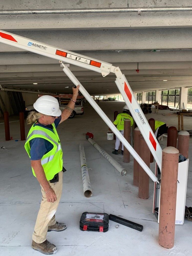Kyosis technician installing a Magnetic Autocontrol barrier gate arm at a parking garage entry lane