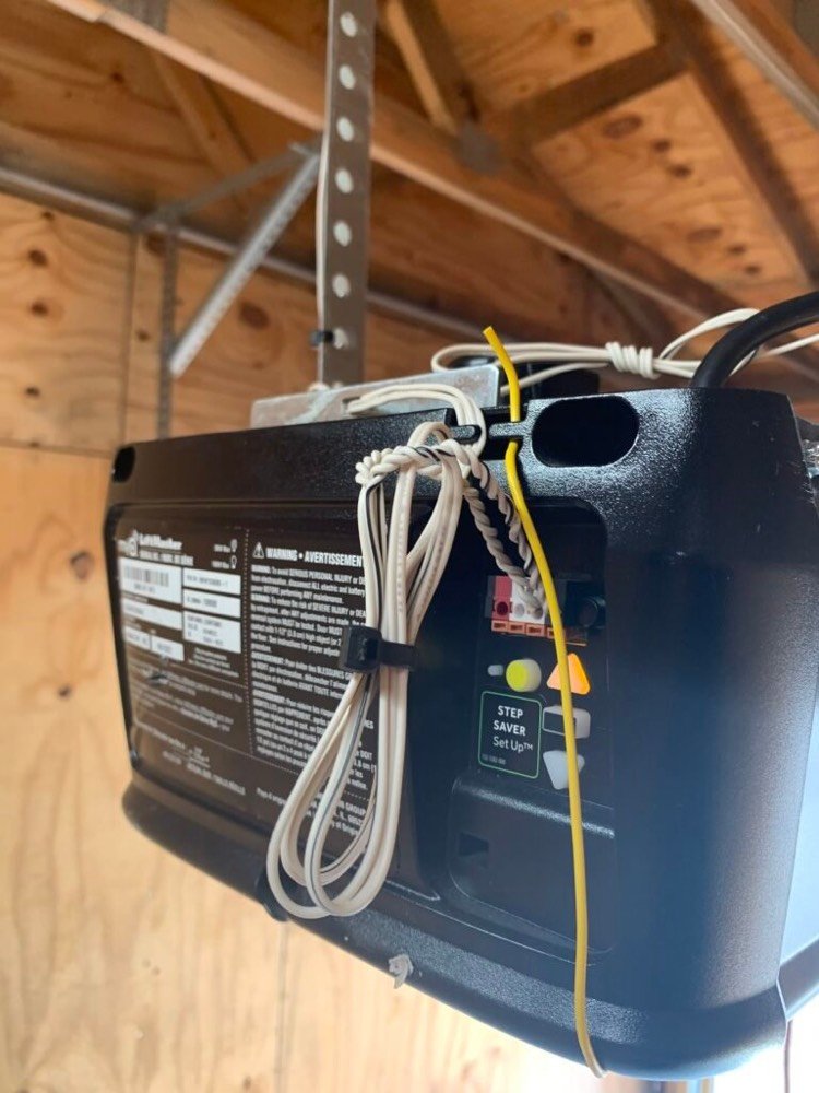 Residential garage door opener unit mounted to ceiling joists with wiring and safety sensor connections